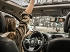 A young woman enjoying a drive with the sunroof open, showing car interior detail.